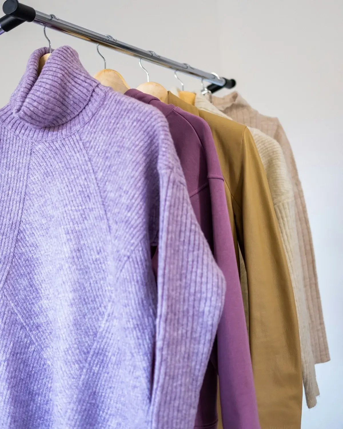 A lavender sweater and purple sweatshirt hanging on a clothing rack