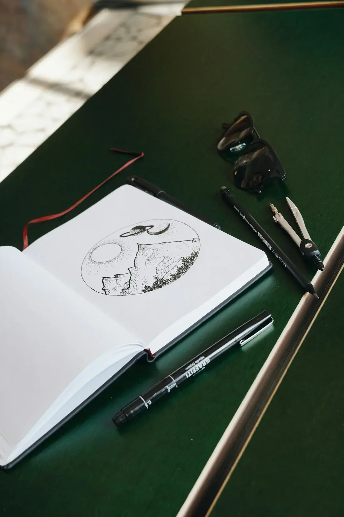 An open sketchbook with a pen drawing of mountains and planets